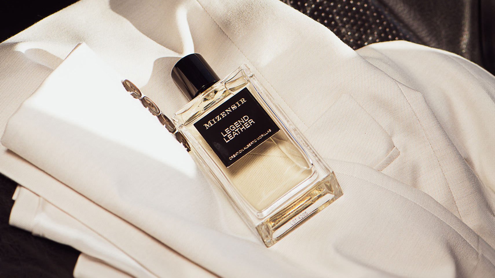 Le parfum cuiré boisé Legend Leather posé sur une veste en coton clair.